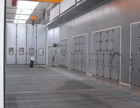  Vista interna della cabina di lavaggio grandi pezzi con quattro gruppi di aspirazione fumane in acciaio inossidabile AISI 304, grigliato totale e sistema di reimmissione aria aspirata con plenum posizionato lateralmente e superiormente alla camera. Nella parete si vedono i portelli per la manutenzione ai gruppi di aspirazione
